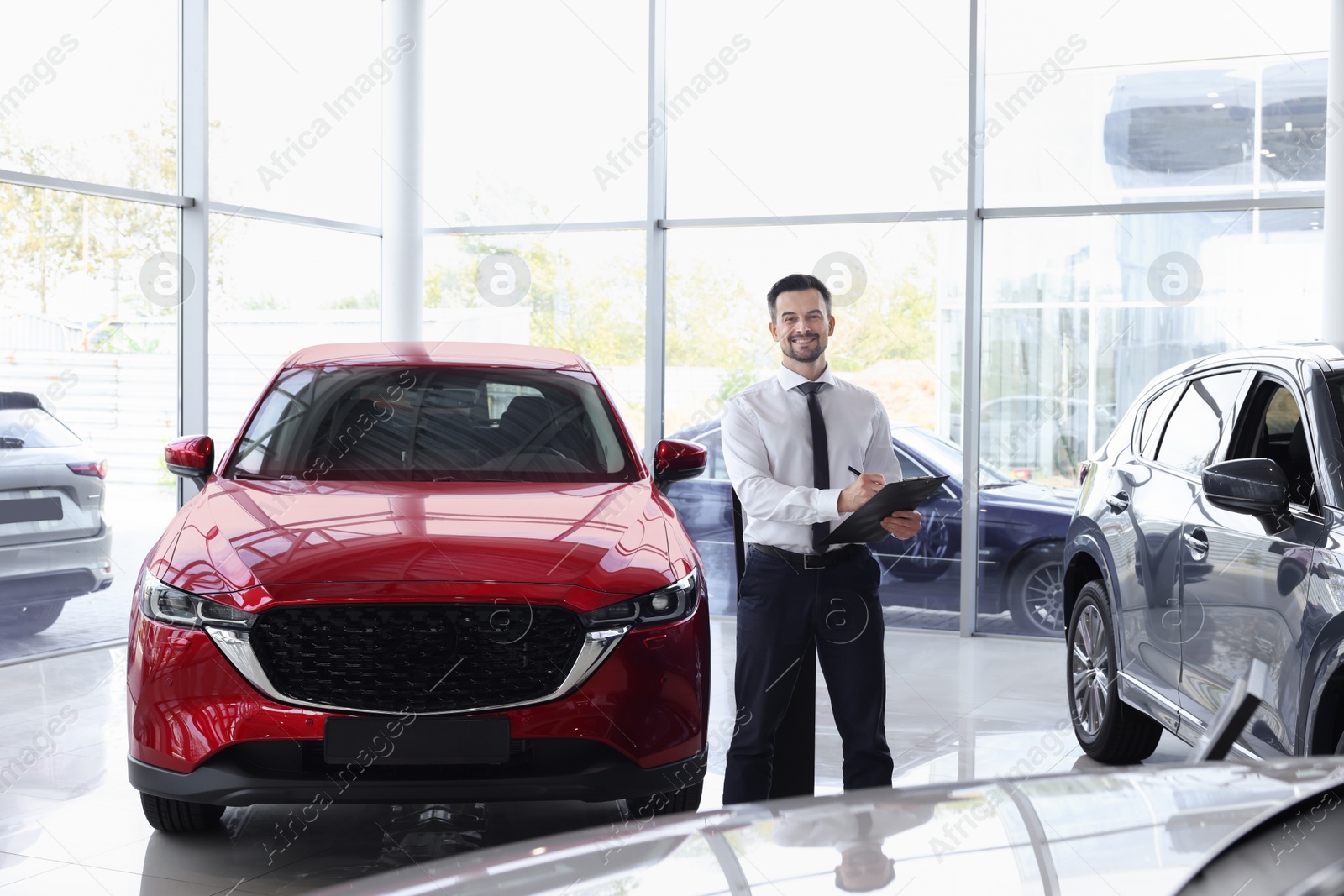 Photo of Happy salesman near new red car in salon