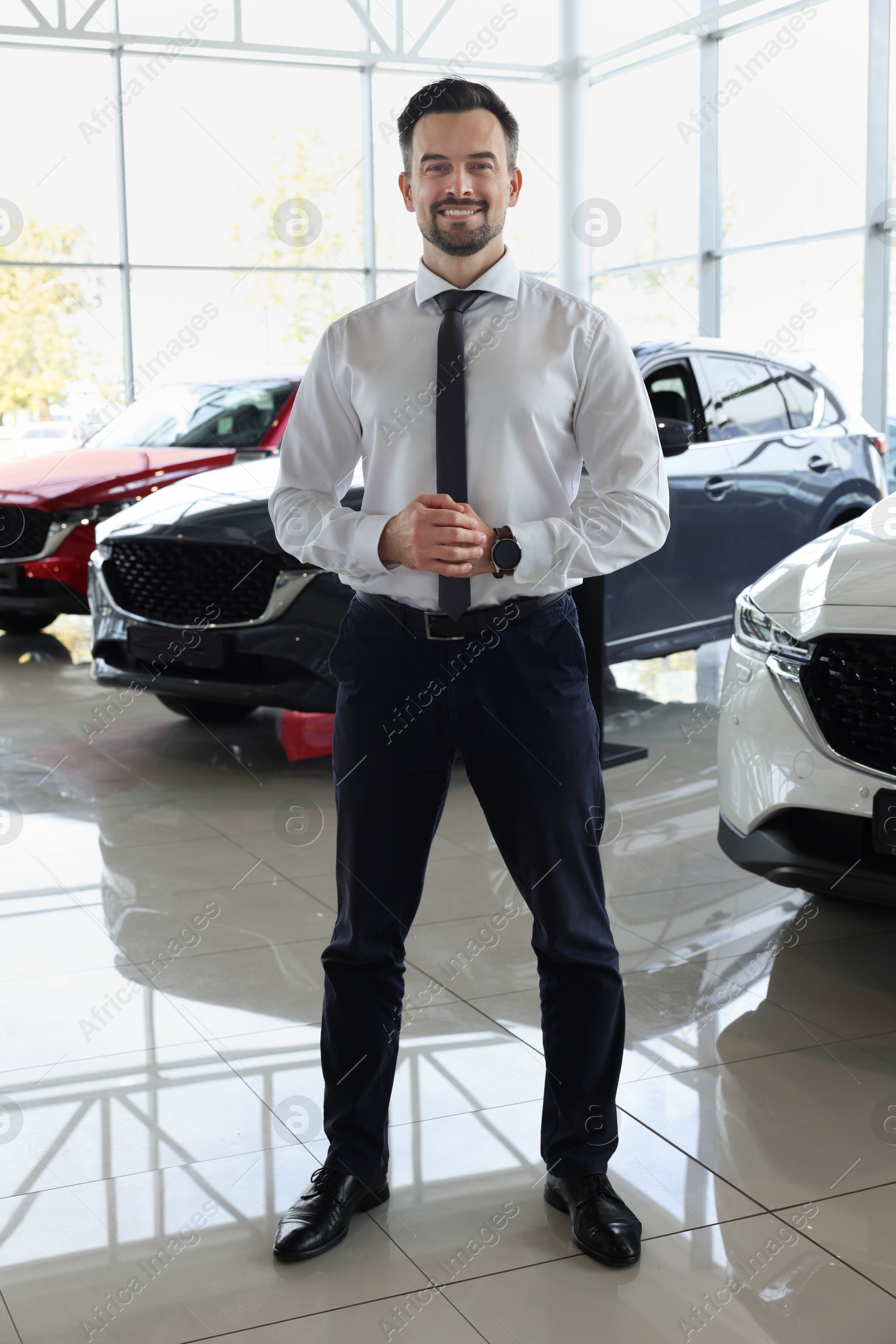 Photo of Happy salesman near new cars in salon