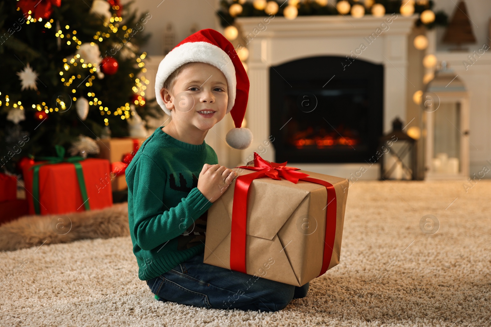 Photo of Cute little boy in Santa hat with Christmas gift indoors