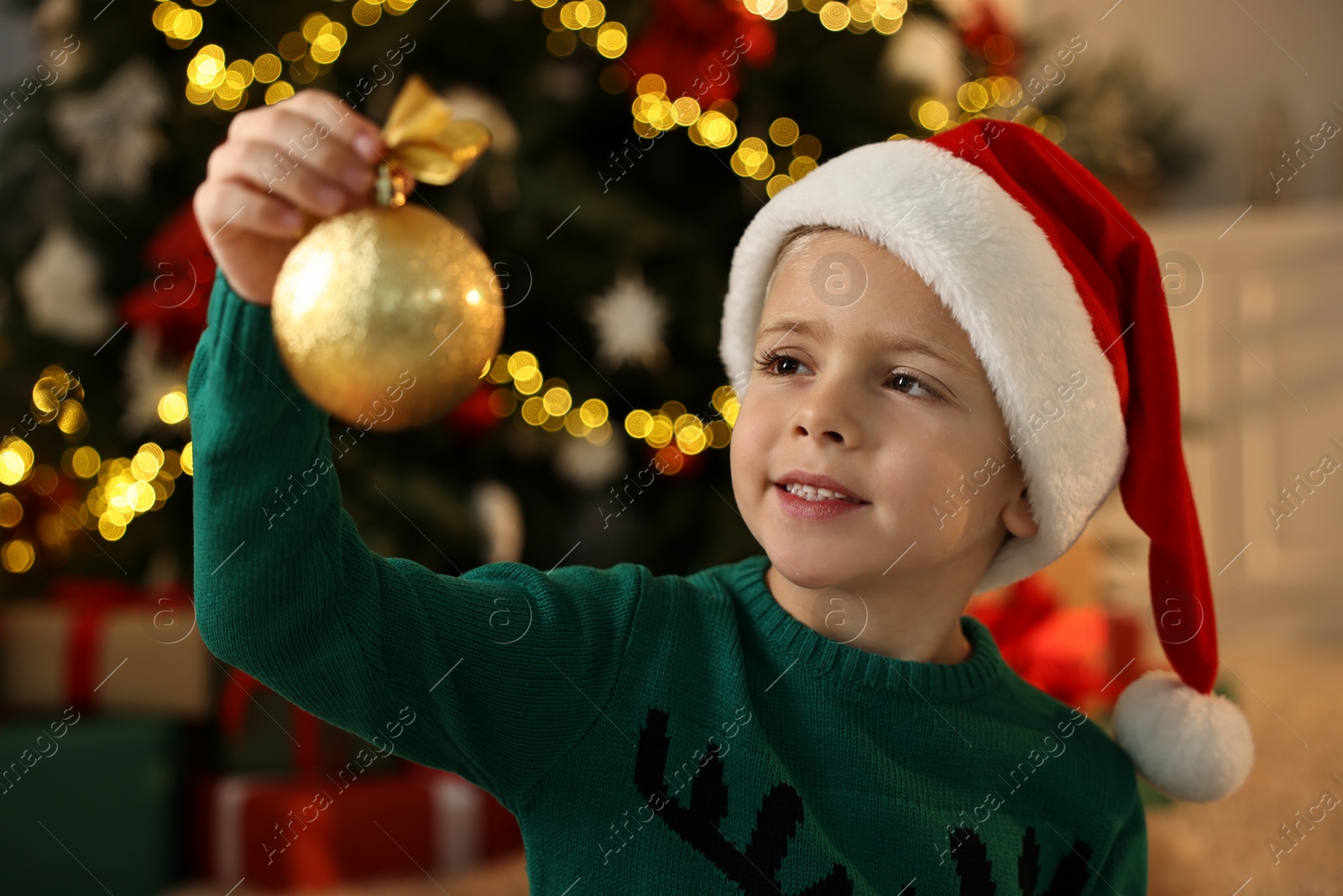 Photo of Cute little boy in Santa hat with Christmas ball at home