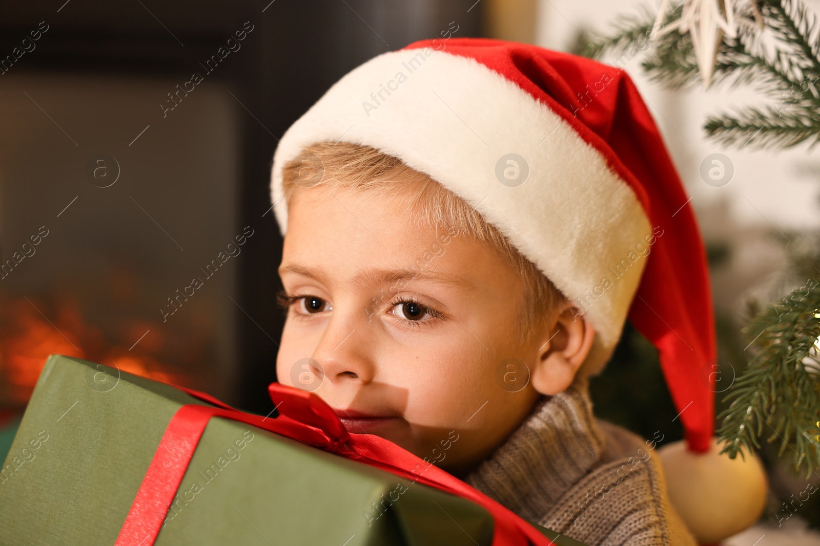 Photo of Little boy in Santa hat with Christmas gift at home