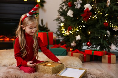 Photo of Little girl opening Christmas gift on floor at home