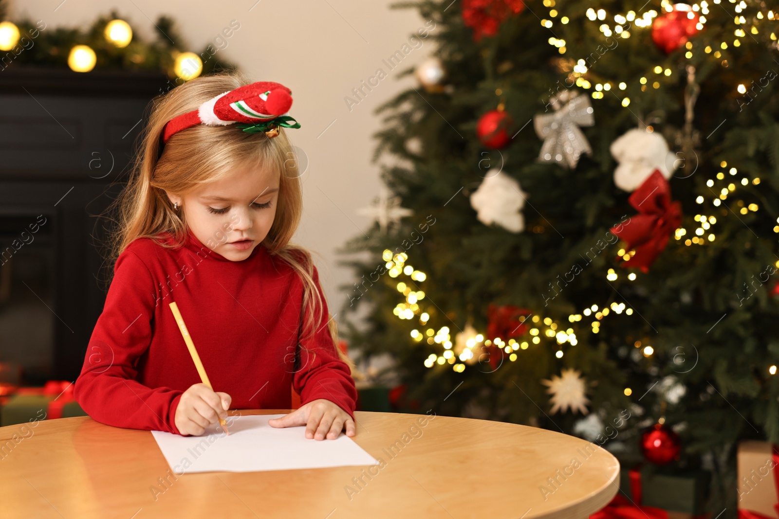 Photo of Little girl writing letter to Santa Claus at table indoors. Christmas celebration