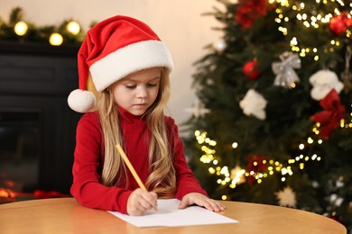 Photo of Little girl writing letter to Santa Claus at table indoors. Christmas celebration