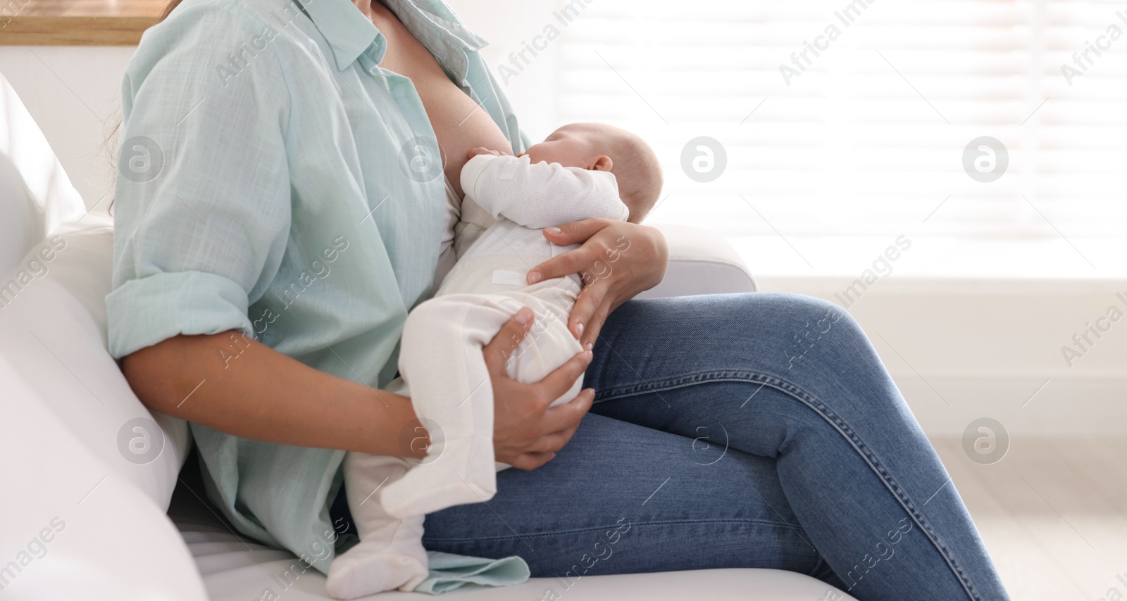 Photo of Mother breastfeeding her little baby on sofa at home, closeup