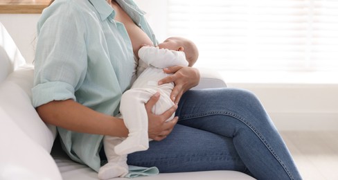 Photo of Mother breastfeeding her little baby on sofa at home, closeup