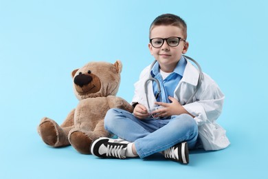 Photo of Little boy with stethoscope and toy pretending to be doctor on light blue background. Dreaming of future profession