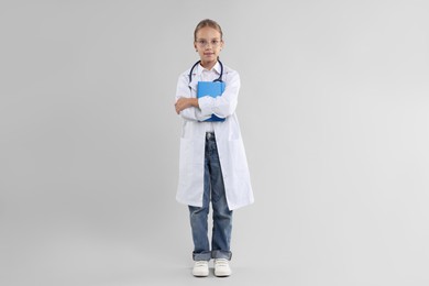 Photo of Girl with stethoscope and book pretending to be doctor on light grey background. Dreaming of future profession