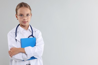 Photo of Girl with stethoscope and book pretending to be doctor on light grey background, space for text. Dreaming of future profession