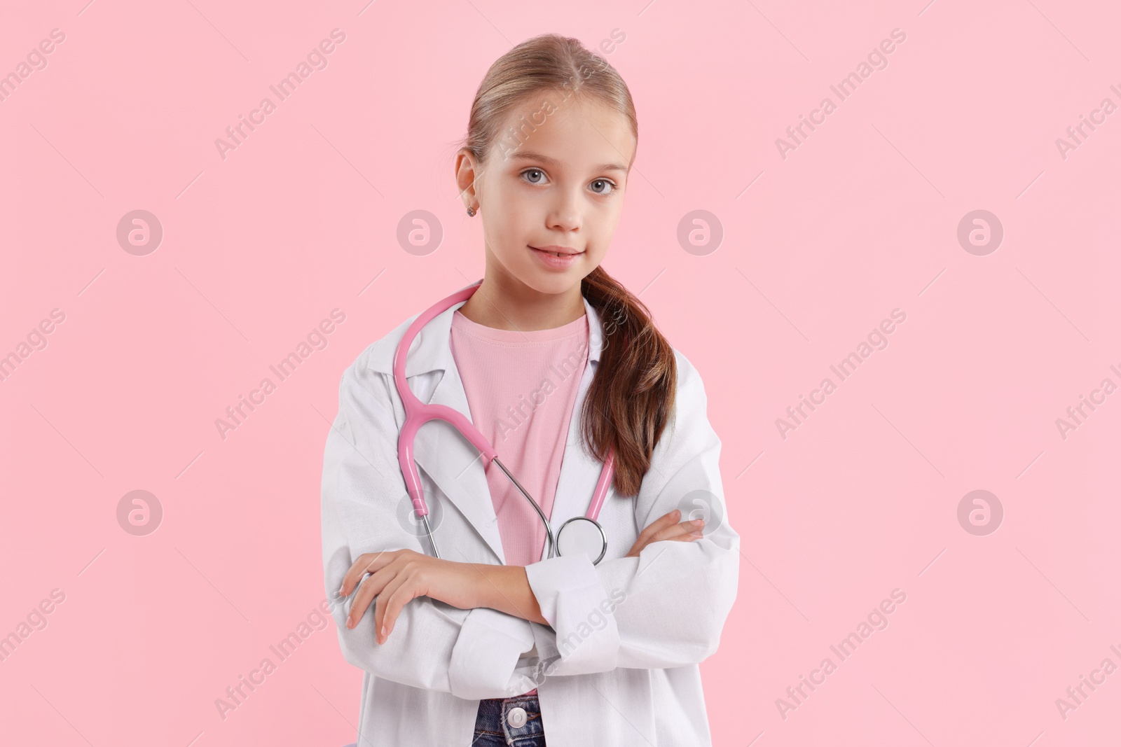 Photo of Girl with stethoscope pretending to be doctor on pink background. Dreaming of future profession