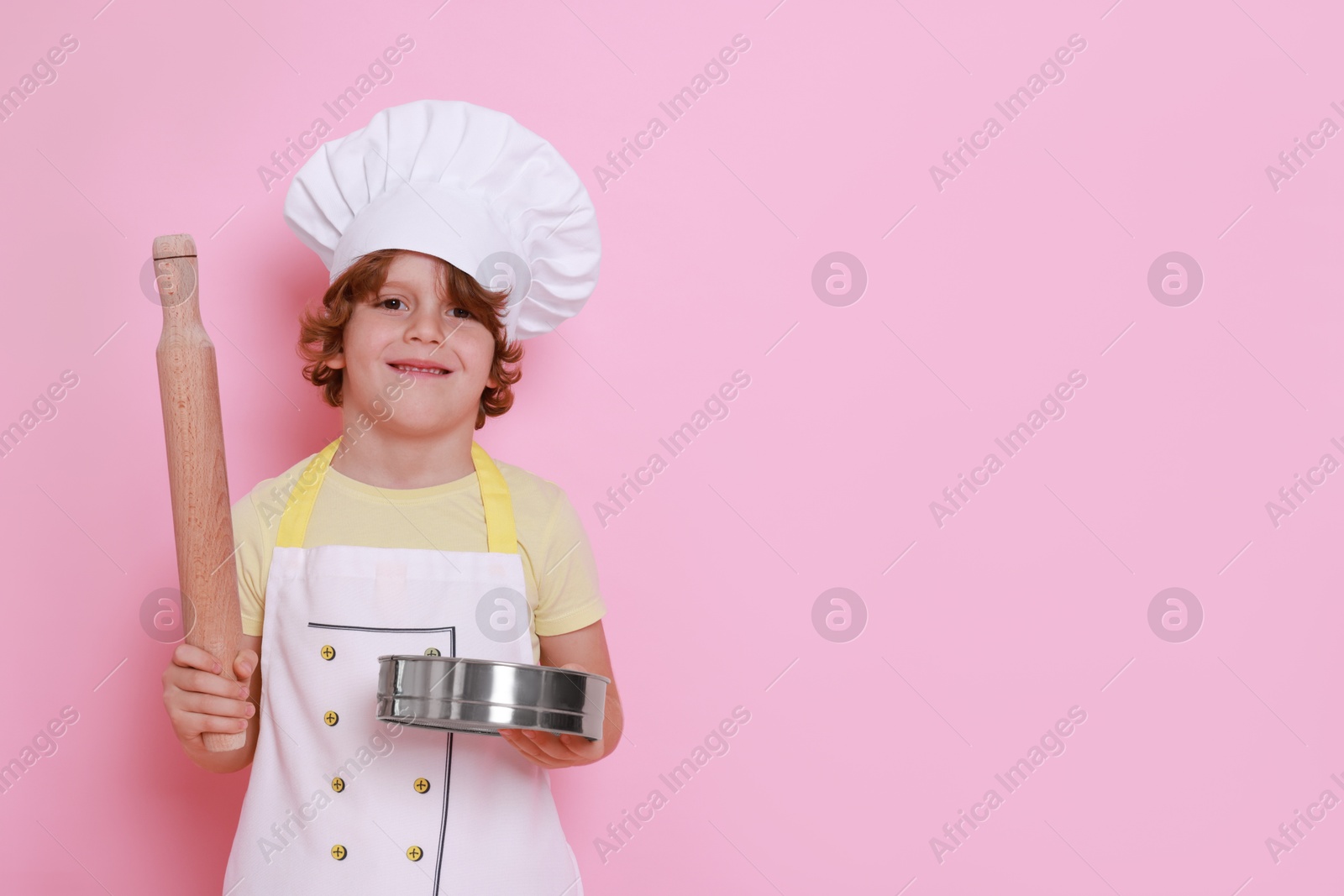 Photo of Little boy with utensils pretending to be chef on pink background, space for text. Dreaming about future profession