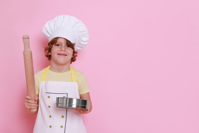 Photo of Little boy with utensils pretending to be chef on pink background, space for text. Dreaming about future profession