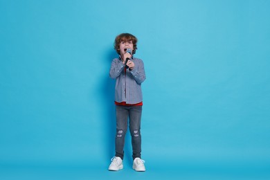 Photo of Little boy with microphone pretending to be singer on light blue background. Dreaming about future profession