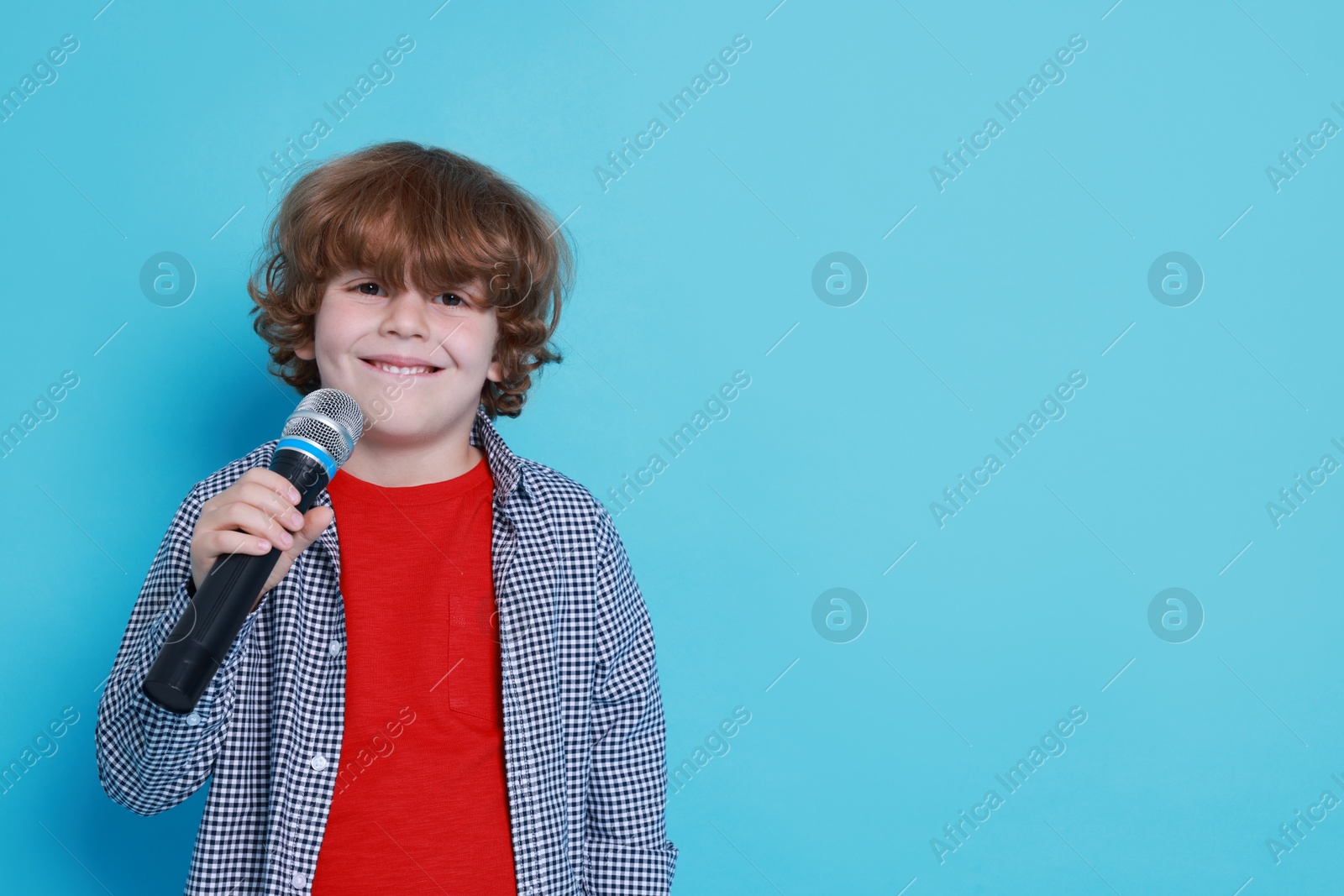 Photo of Little boy with microphone pretending to be singer on light blue background, space for text. Dreaming about future profession