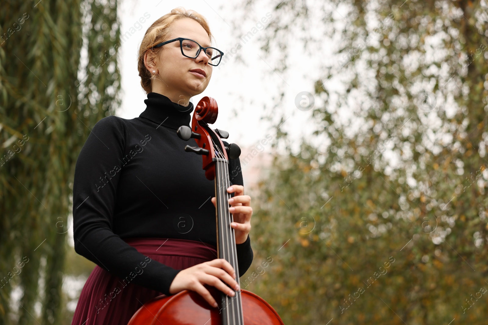 Photo of Beautiful young woman with cello outdoors, low angle view. Space for text