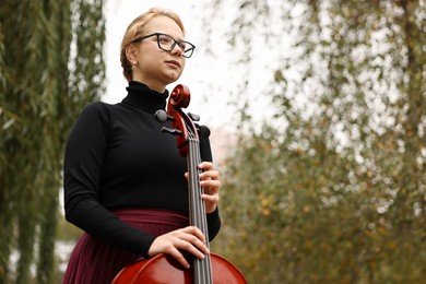 Photo of Beautiful young woman with cello outdoors, low angle view. Space for text