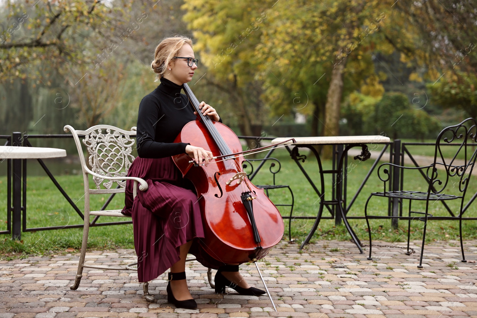 Photo of Beautiful young woman playing cello in park, space for text