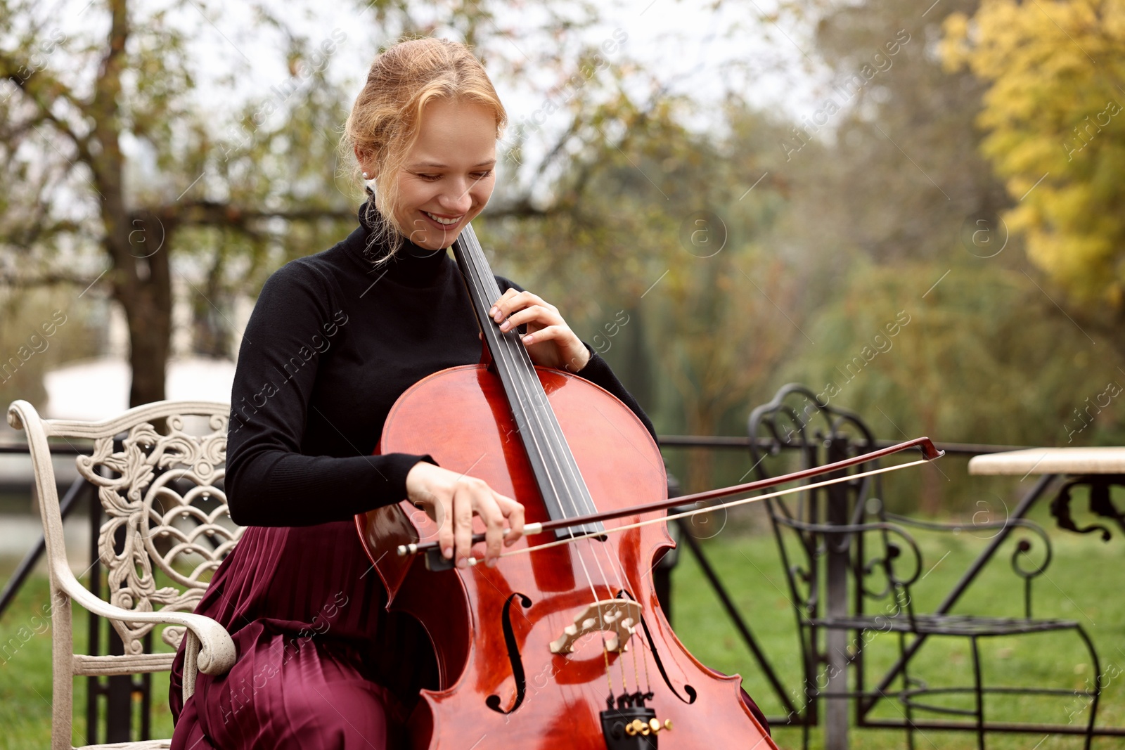 Photo of Beautiful young woman playing cello in park, space for text