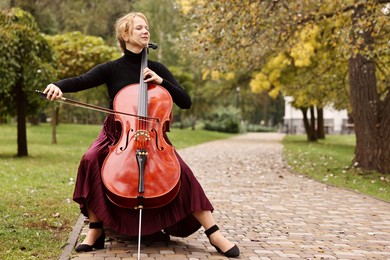 Photo of Beautiful young woman playing cello in park, space for text