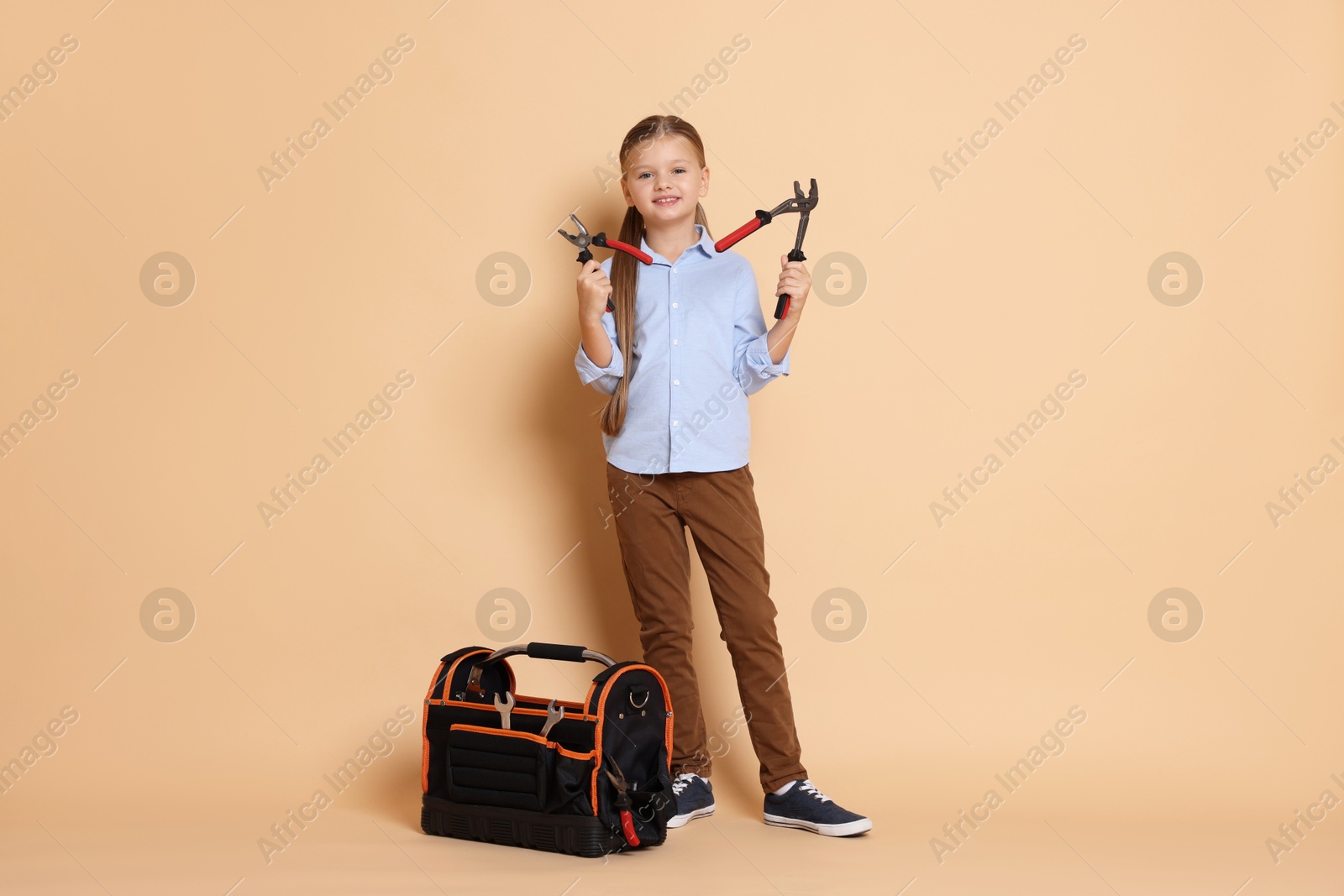 Photo of Little girl with tools on beige background. Dreaming about future profession