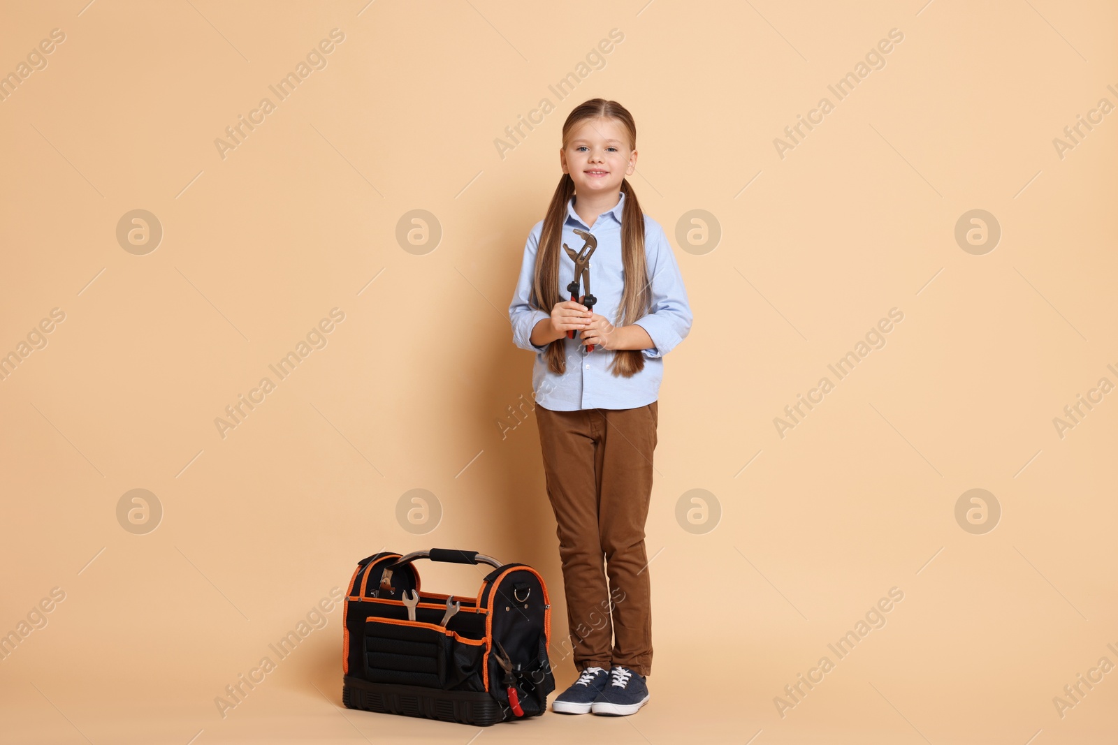 Photo of Little girl with tools on beige background. Dreaming about future profession