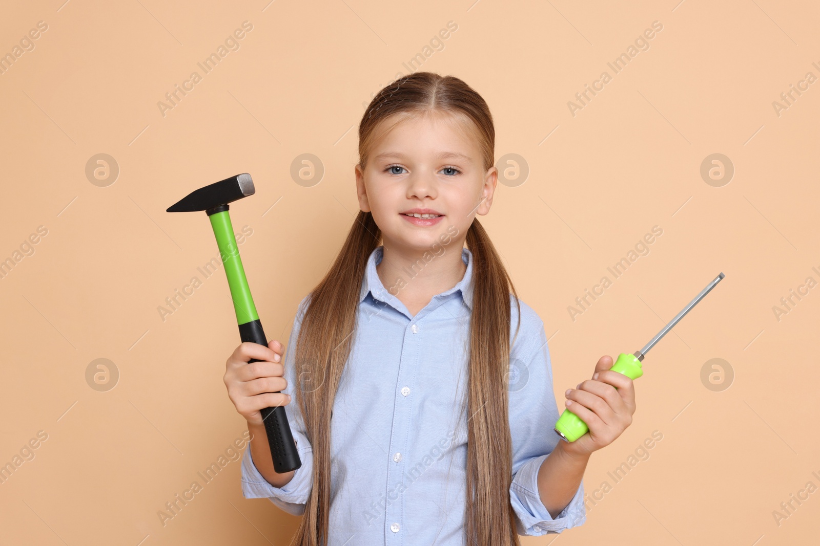 Photo of Little girl with hammer and screwdriver on beige background. Dreaming about future profession