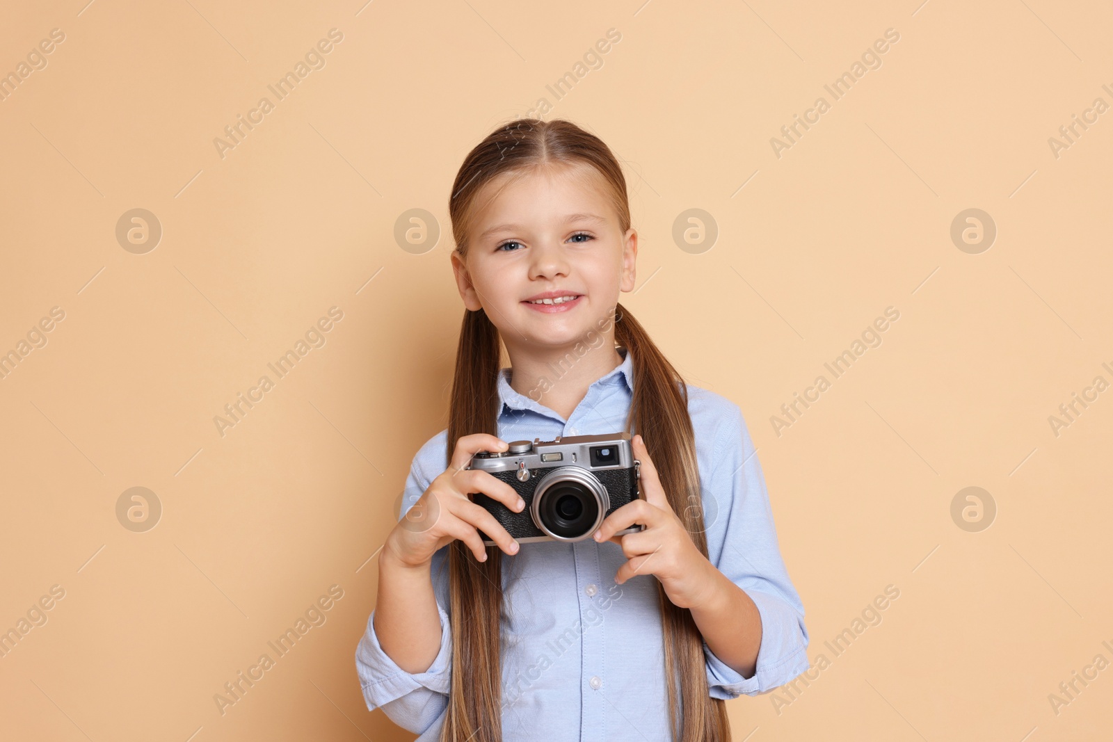 Photo of Little girl with camera pretending to be photographer on beige background. Dreaming of future profession