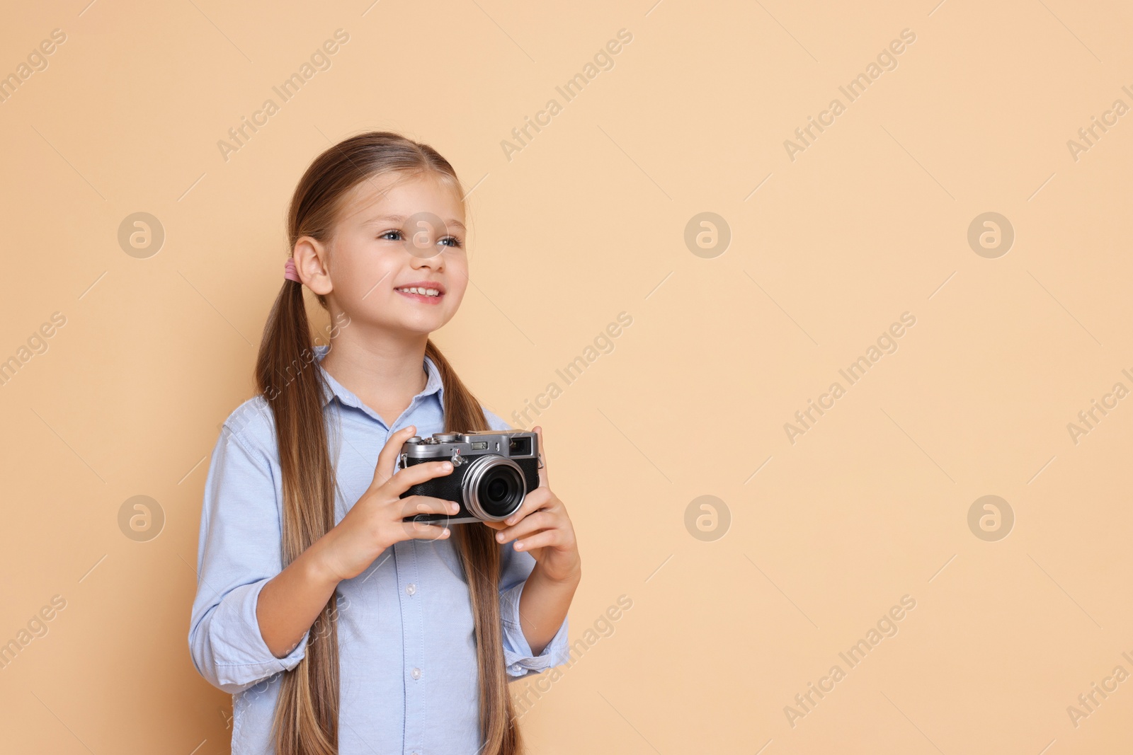 Photo of Little girl with camera pretending to be photographer on beige background, space for text. Dreaming of future profession