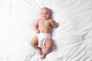 Photo of Cute little baby in diaper on bed, top view