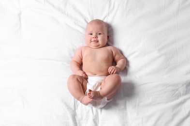 Photo of Cute little baby in diaper on bed, top view