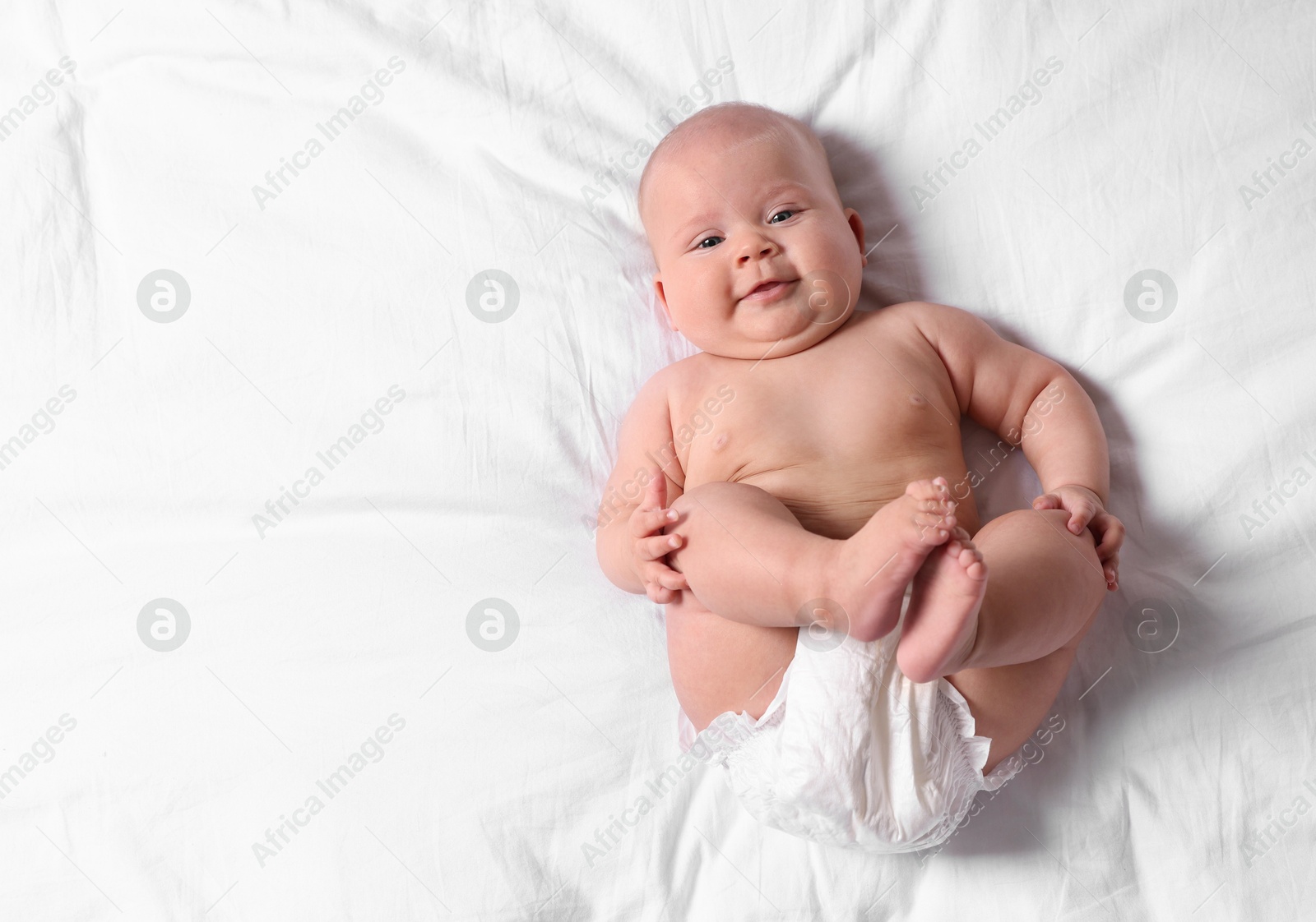 Photo of Cute little baby in diaper on bed, top view. Space for text