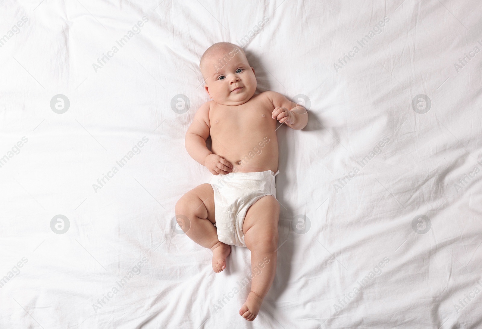 Photo of Cute little baby in diaper on bed, top view