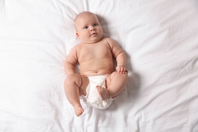 Photo of Cute little baby in diaper on bed, top view