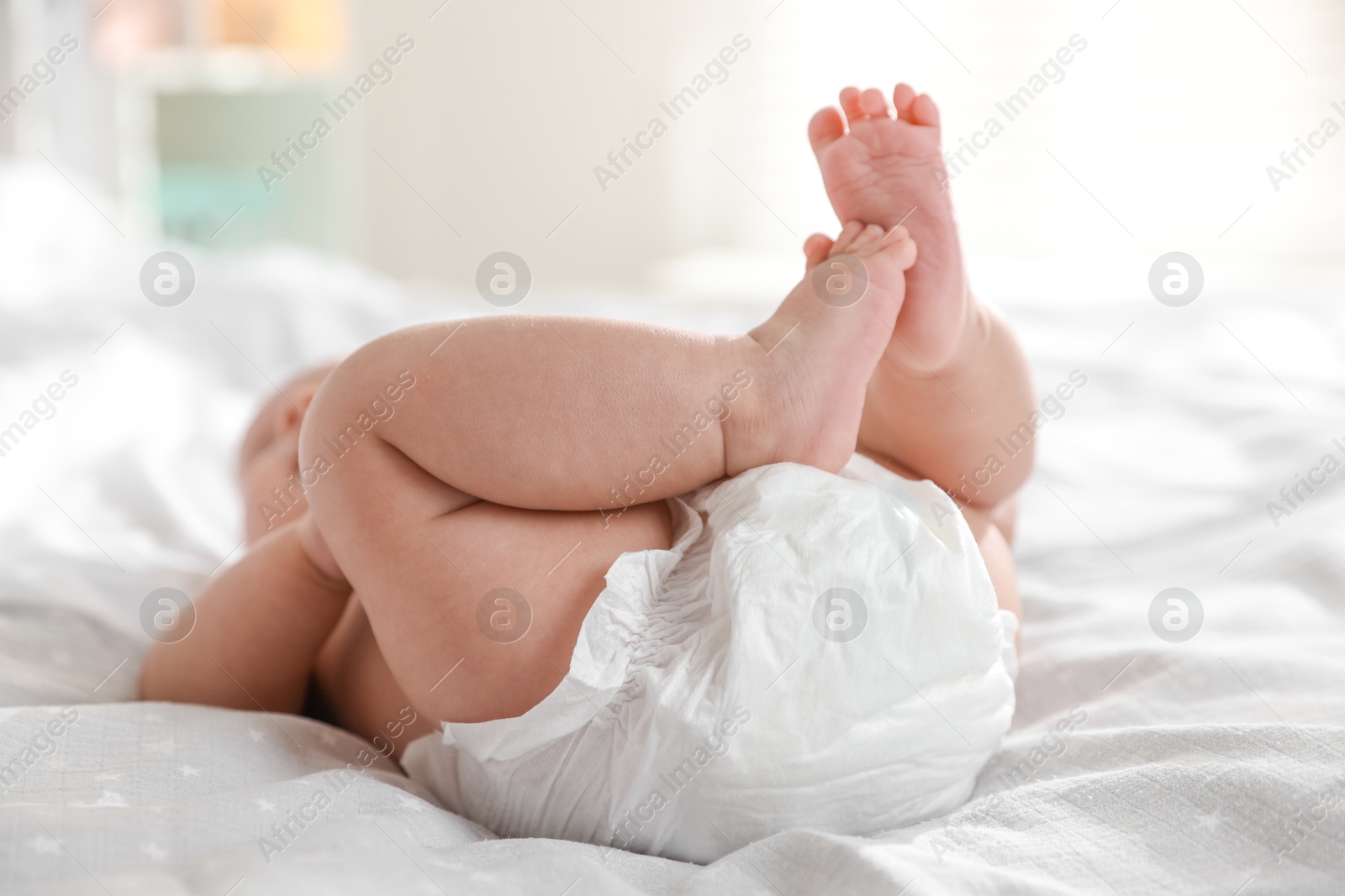 Photo of Cute little baby in diaper on bed indoors, closeup