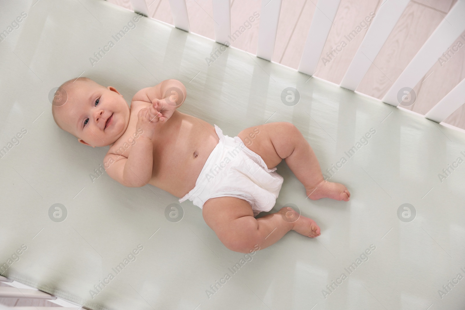 Photo of Cute little baby wearing diaper in crib, top view