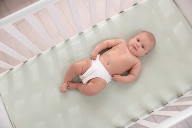 Photo of Cute little baby wearing diaper in crib, top view