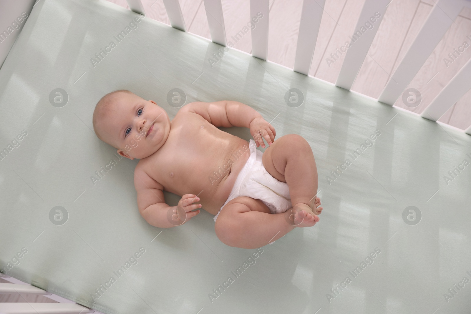 Photo of Cute little baby wearing diaper in crib, top view