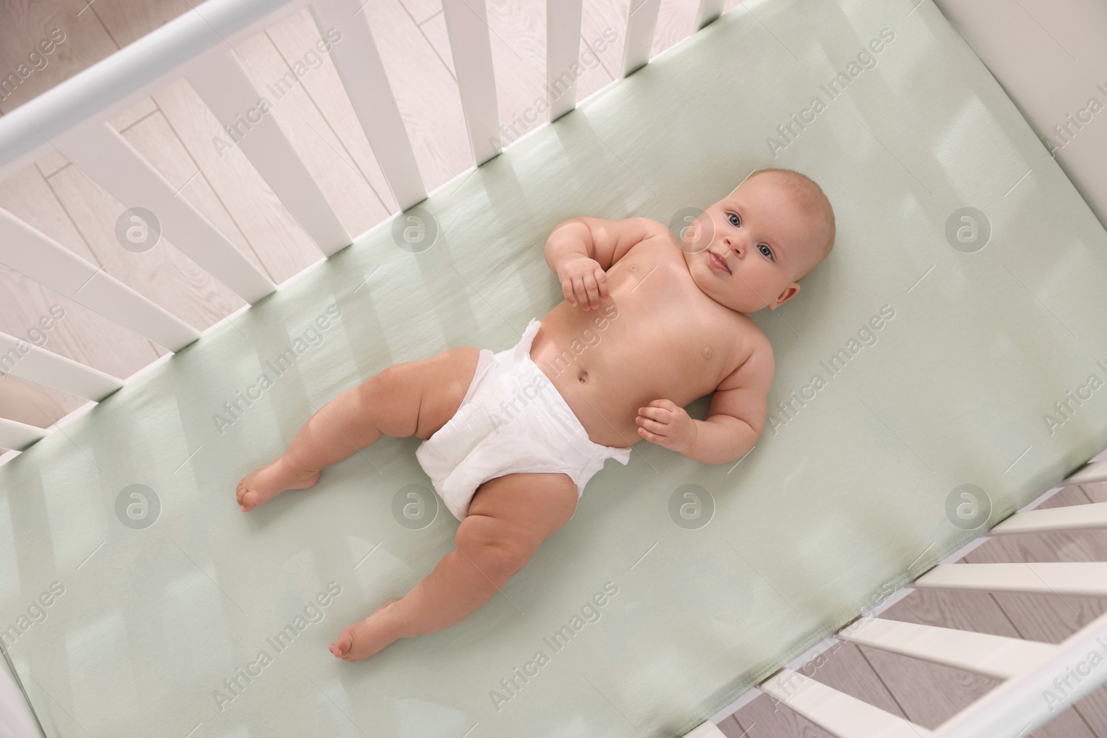 Photo of Cute little baby wearing diaper in crib, top view