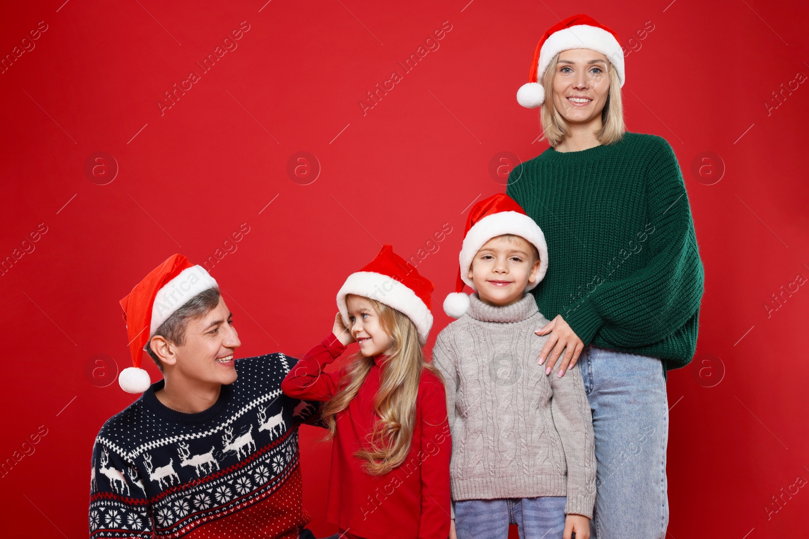 Photo of Happy family in Santa hats on red background. Christmas season