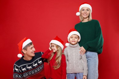 Photo of Happy family in Santa hats on red background. Christmas season