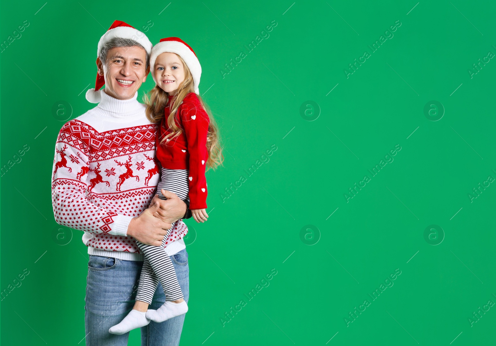 Photo of Father and daughter in Santa hats on green background, space for text. Christmas celebration