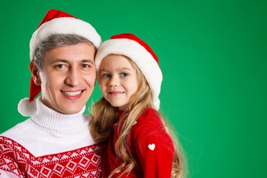 Photo of Father and daughter in Santa hats on green background, space for text. Christmas celebration