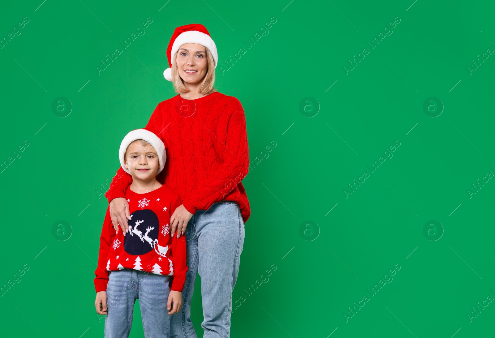 Photo of Mother and son in Santa hats on green background, space for text. Christmas celebration