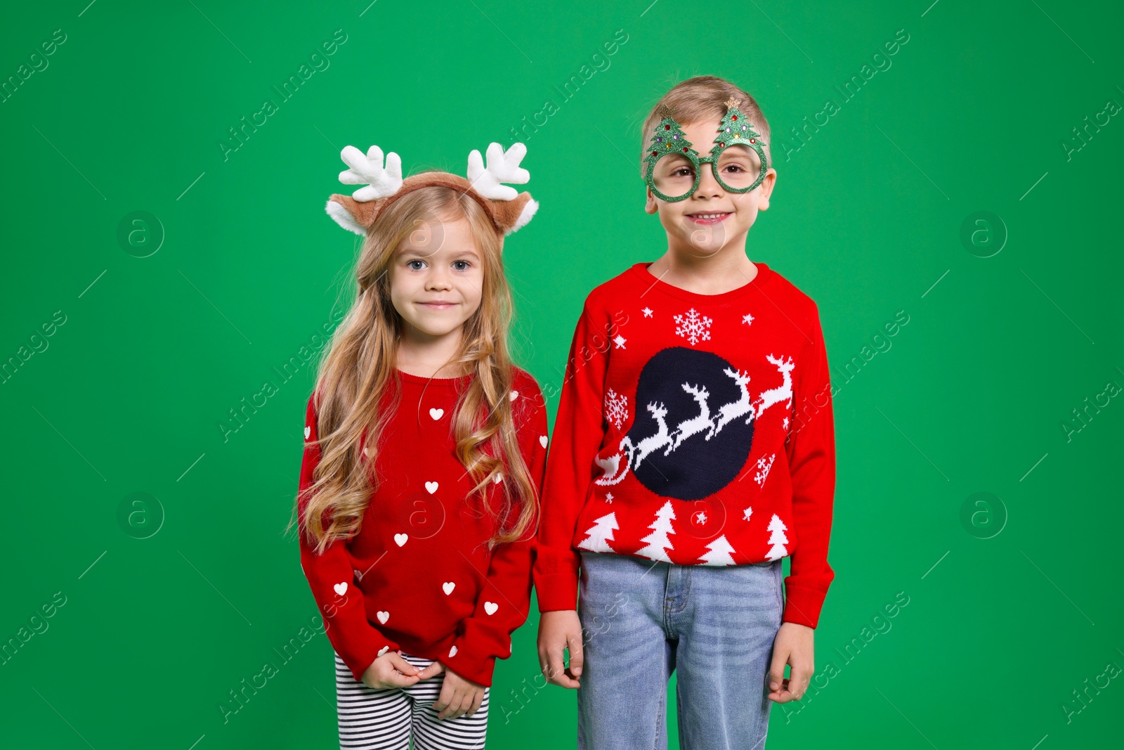 Photo of Cute little children in Christmas sweaters and accessories on green background