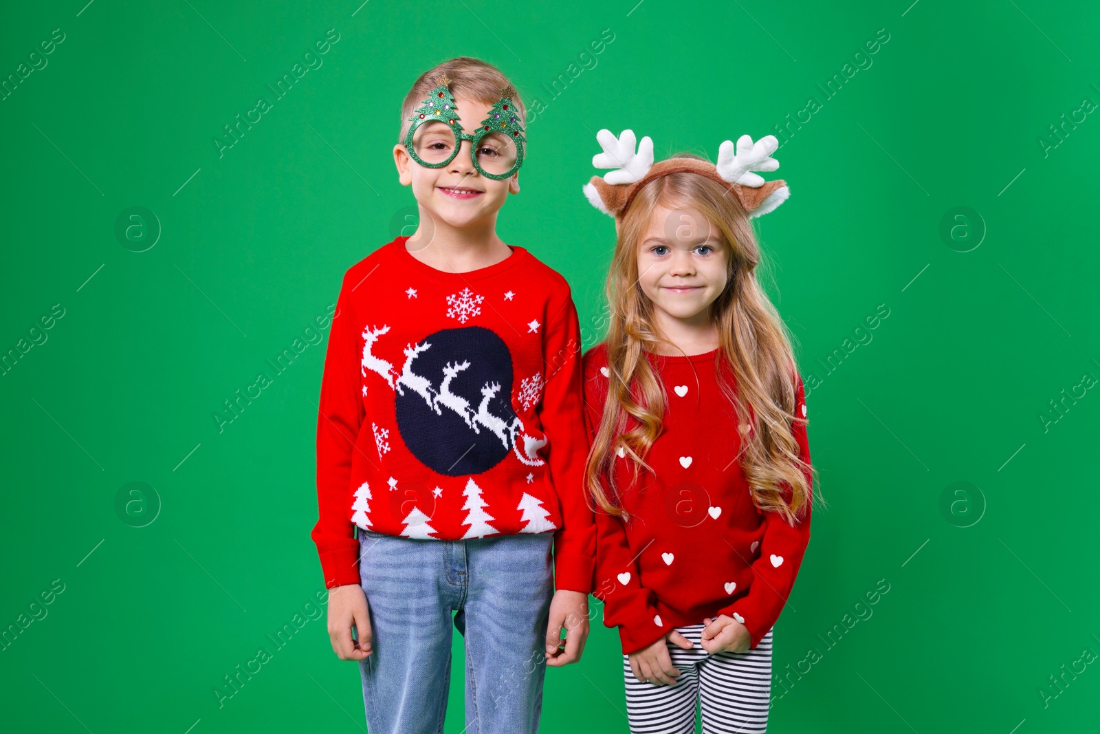 Photo of Cute little children in Christmas sweaters and accessories on green background