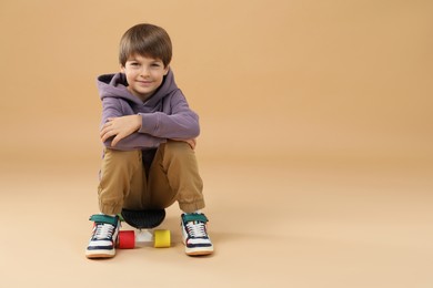 Photo of Little boy with skateboard on beige background, space for text