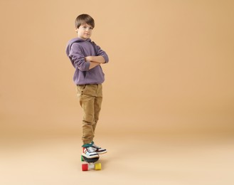 Photo of Little boy with skateboard on beige background, space for text