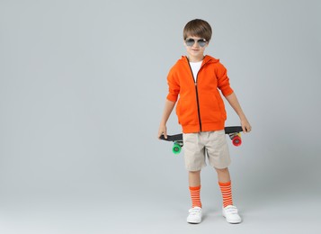 Photo of Little boy with skateboard on light grey background, space for text