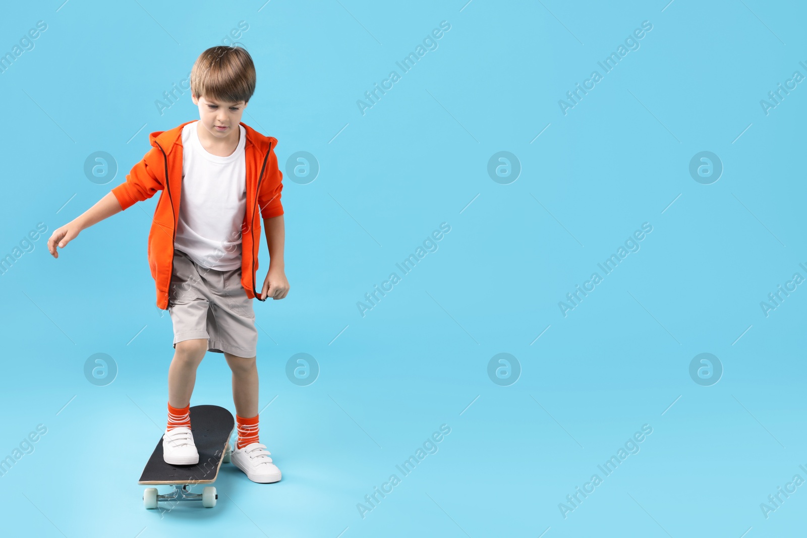 Photo of Little boy with skateboard on light blue background, space for text