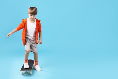 Photo of Little boy with skateboard on light blue background, space for text